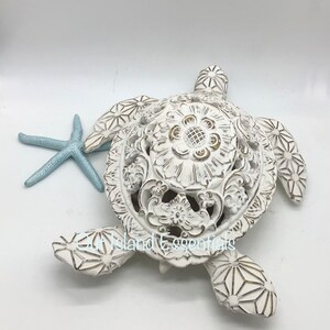 May include: White ceramic turtle sculpture with intricate carved details. The turtle has a detailed floral design on its shell and a starfish beside it.