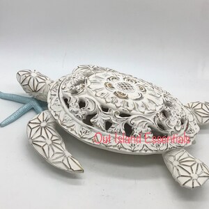 May include: White ceramic sea turtle sculpture with intricate details and a light blue starfish. The turtle's shell has a floral design and is slightly open.