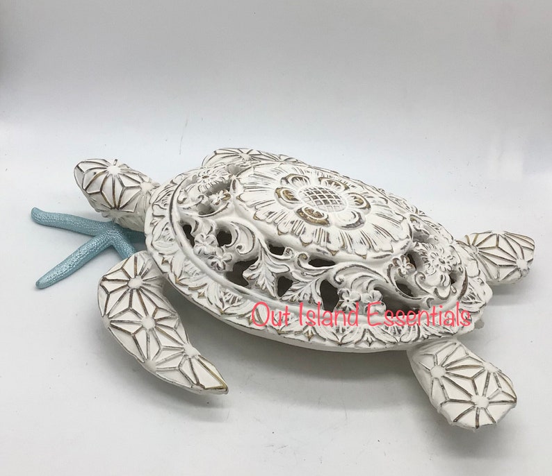 May include: White ceramic sea turtle sculpture with intricate details and a light blue starfish. The turtle's shell has a floral design and is slightly open.