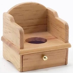 May include: A miniature wooden chair with a round opening and a small drawer. The chair has a curved back and armrests. The drawer has a small, round, gold-colored knob. The wood has a natural, light brown color.