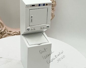 May include: White miniature washer and dryer set. The dryer is stacked on top of the washer. The washer has a small lid. The set is on a white surface with a handwritten note that says "Out Island Essentials xoxo".