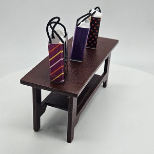 May include: Three miniature Halloween-themed gift bags with black handles sit on a dark brown wooden table. The bags are decorated with stripes, spiderwebs, and polka dots.