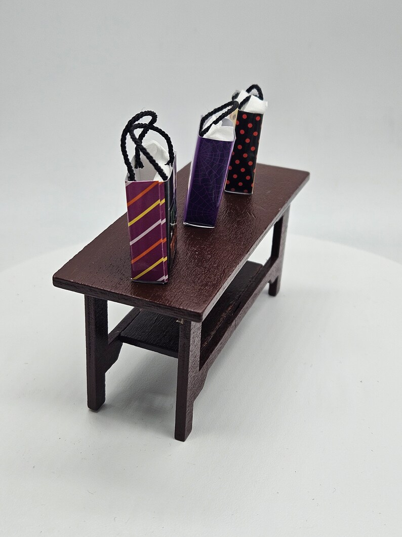 May include: Three miniature Halloween-themed gift bags with black handles sit on a dark brown wooden table. The bags are decorated with stripes, spiderwebs, and polka dots.
