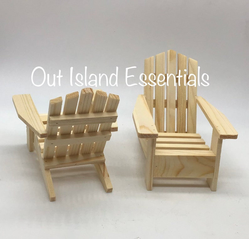 Puede incluir: Dos sillas Adirondack de madera sin terminar. Las sillas son de madera natural y tienen un dise&ntilde;o sencillo.  Out Island Essentials est&aacute; impreso en la imagen.