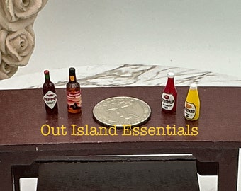 May include: A set of miniature glass bottles with labels. The bottles contain condiments such as ketchup, mustard, and hot sauce. The bottles are arranged on a wooden surface. Out Island Essentials is written on the surface.