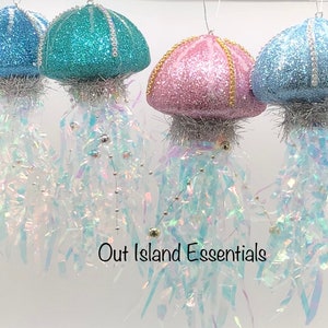 May include: Four glittery jellyfish Christmas ornaments with iridescent tails. The jellyfish are blue, teal, pink, and light blue.