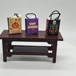 May include: Three miniature Halloween-themed gift bags with black handles. The bags are decorated with different designs: a jack-o-lantern, "Happy Haunting", and "Trick or Treat" with a skull.