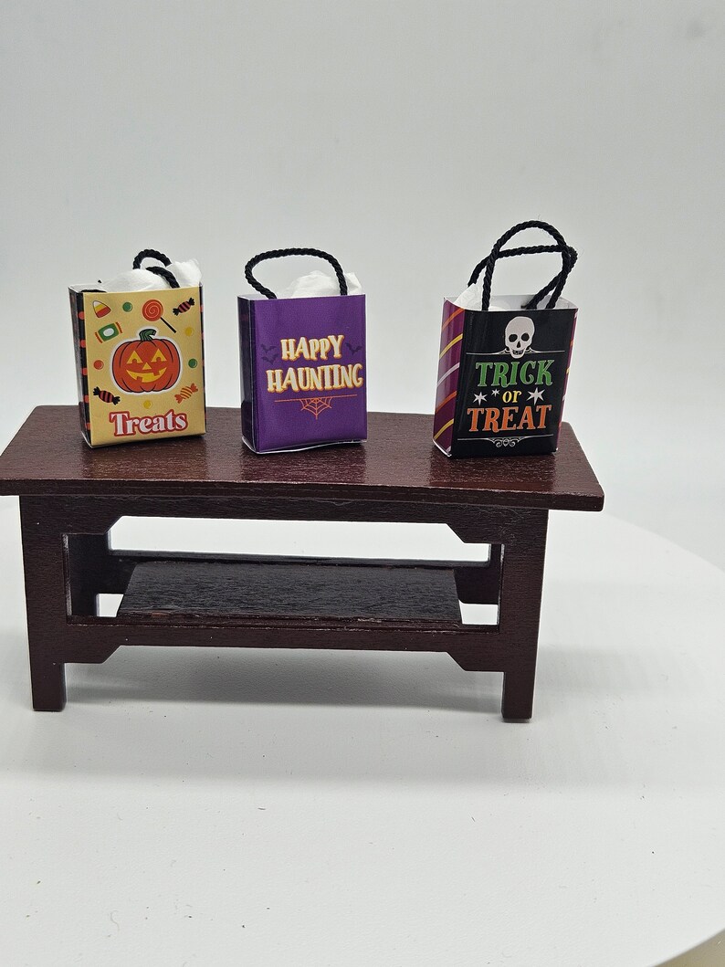May include: Three miniature Halloween-themed gift bags with black handles. The bags are decorated with different designs: a jack-o-lantern, "Happy Haunting", and "Trick or Treat" with a skull.