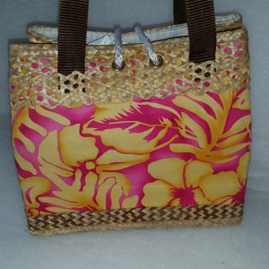 Puede incluir: Un peque&ntilde;o bolso de paja con asas marrones y estampado floral. El estampado presenta flores rosas y amarillas sobre un fondo amarillo.