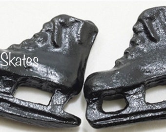Puede incluir: Dos abalorios de patines de hielo negros con un acabado brillante. Los abalorios están detallados con cordones y cuchillas. El texto "IceSkates" es visible en uno de los abalorios.