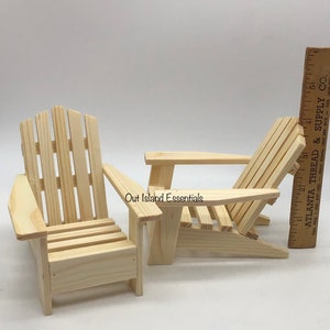 Puede incluir: Dos sillas Adirondack de madera sin terminar, una est&aacute; derecha y la otra est&aacute; reclinada. Las sillas son de madera natural y tienen aproximadamente 38 cm de altura.