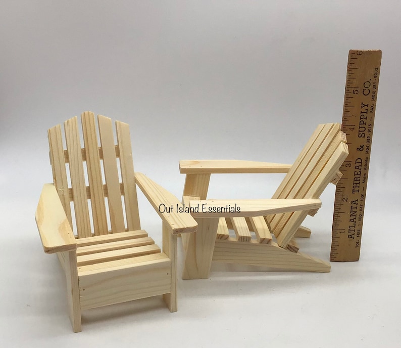 Puede incluir: Dos sillas Adirondack de madera sin terminar, una est&aacute; derecha y la otra est&aacute; reclinada. Las sillas son de madera natural y tienen aproximadamente 38 cm de altura.