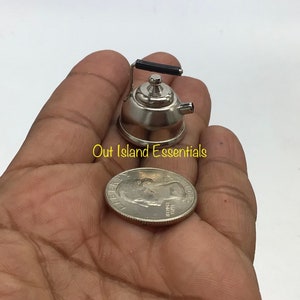Peut inclure: Une petite théière en argent miniature avec une poignée noire. La théière est à peu près de la taille d'une pièce de 25 centimes d'euro.
