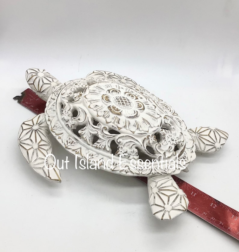 May include: White ceramic turtle sculpture with intricate carvings and a distressed finish. The turtle's shell features a large, detailed floral design with a gold accent.