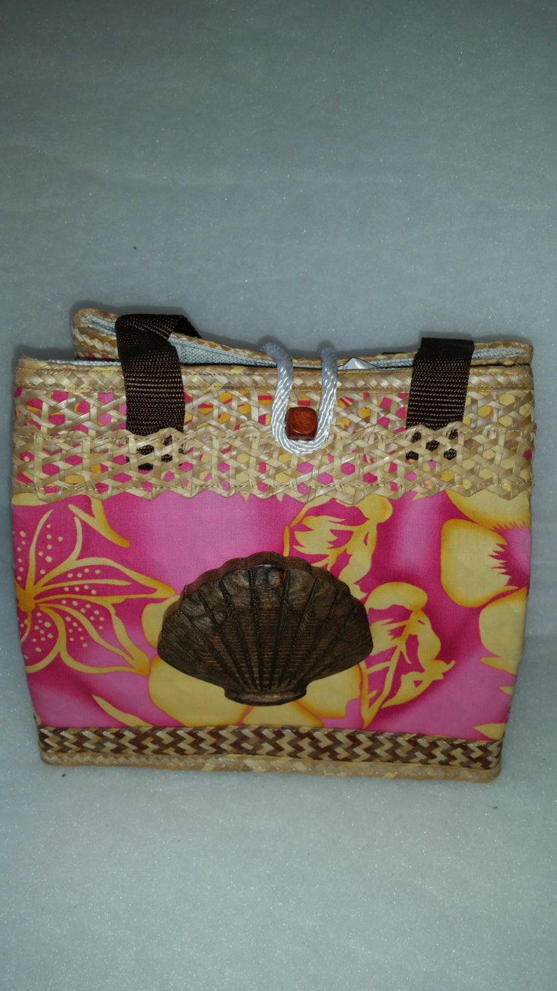 Puede incluir: Un bolso de mano floral rosa y amarillo con un dise&ntilde;o de concha marr&oacute;n. El bolso est&aacute; hecho de paja tejida y tiene asas marrones.