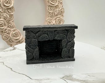 Może przedstawiać: Miniaturowy kominek z kamienia z czarnym wykończeniem. Kominek ma prostokątny otwór i szorstką strukturę kamienia.