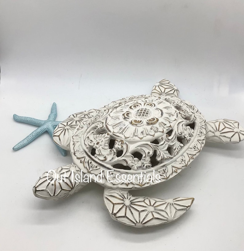 May include: White ceramic turtle sculpture with intricate floral designs and gold accents. The turtle is lying on its back with its legs outstretched. A blue starfish is next to the turtle.