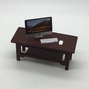 May include: A miniature wooden desk with a dark brown finish. A silver computer monitor with a landscape image on the screen, a white keyboard, and a white mouse are on the desk.