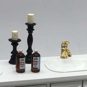 May include: Two black candle holders with white candles, two bottles of hydrogen peroxide solution, and a gold faucet on a white countertop.