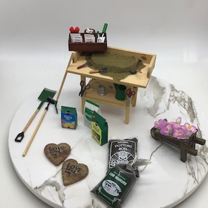 Puede incluir: Un conjunto de jardinería en miniatura con una mesa de madera, una carretilla, herramientas de jardinería y bolsas de tierra para macetas, estiércol de vaca y mezcla para macetas. La mesa tiene un pequeño estante de madera y un letrero que dice "Zinnia, Guisantes, Dailey".