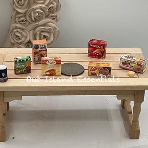 Könnte beinhalten: Miniatur-Lebensmittel auf einem hellen Holztisch. Enthält Schachteln mit Hot Roll, Fruit Burst, Chocolate Gems, Eggo-Waffeln und Hot Pockets. Ein kleiner Morton-Salzbehälter und eine Metallscheibe sind ebenfalls vorhanden.