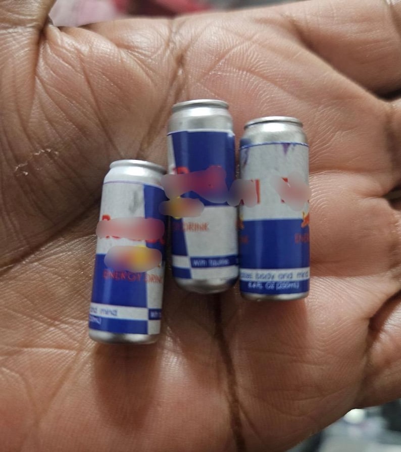 May include: Three small Red Bull energy drink cans. The cans are silver with blue and red branding. The text "ENERGY DRINK" is visible on one can. Each can is approximately 3 inches tall.