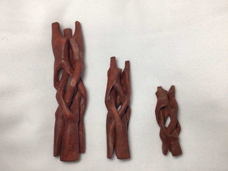 Op de afbeelding: Drie houten sculpturen van in elkaar verweven takken, elk met een andere grootte. De sculpturen zijn roodbruin van kleur en hebben een gladde, gepolijste afwerking.