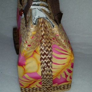 Puede incluir: Un bolso tejido marr&oacute;n y amarillo con un estampado floral rosa y correas marrones.
