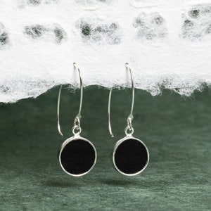 May include: A pair of silver dangle earrings with black round discs. The earrings have a simple design and are perfect for everyday wear.