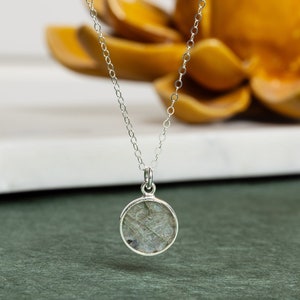 May include: A silver chain necklace with a round pendant featuring a grey and white stone.