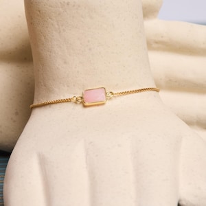 May include: A delicate gold chain bracelet with a single pink rectangular gemstone.