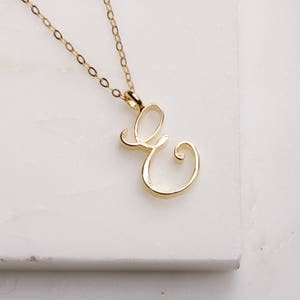 May include: A gold chain necklace with a delicate cursive letter 'E' pendant.