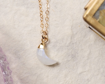 May include: A gold chain necklace with a crescent moon pendant made of white moonstone.