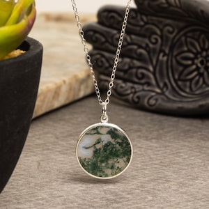 May include: A silver chain necklace with a round pendant featuring a green and white moss agate stone.