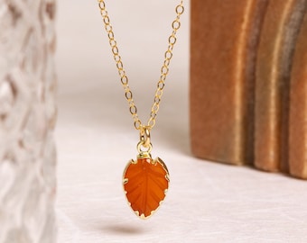 May include: A gold chain necklace with a carved orange leaf pendant.