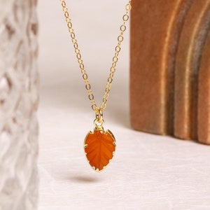 May include: A gold chain necklace with a carved orange leaf pendant.