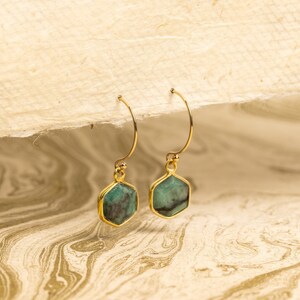 May include: A pair of gold hoop earrings with green gemstone hexagon-shaped pendants.