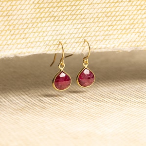 May include: A pair of gold dangle earrings with teardrop-shaped red ruby stones.