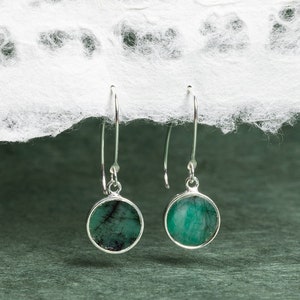 May include: A pair of silver dangle earrings with round green emerald stones.