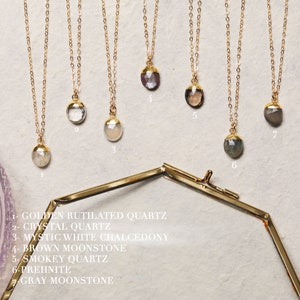 May include: Seven gold necklaces with different gemstone pendants. The pendants are: golden rutilated quartz, crystal quartz, mystic white chalcedony, brown moonstone, smokey quartz, prehnite, and gray moonstone.
