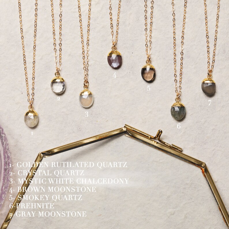 May include: Seven gold necklaces with different gemstone pendants. The pendants are: golden rutilated quartz, crystal quartz, mystic white chalcedony, brown moonstone, smokey quartz, prehnite, and gray moonstone.
