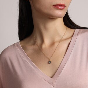 May include: A gold chain necklace with a dark gray gemstone pendant. The pendant is a faceted, round shape.