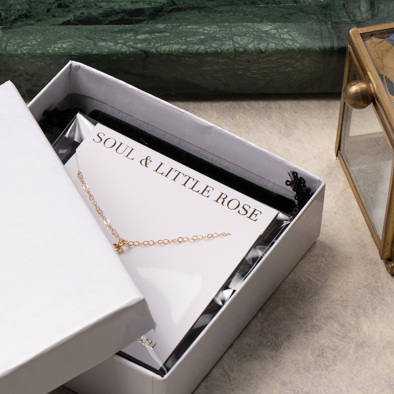 May include: A white box with a gold chain necklace inside. The box has a black velvet lining and a white card with the text "SOUL & LITTLE ROSE" printed on it.