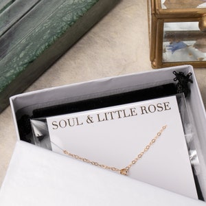 May include: A white box with a black velvet lining and a gold chain necklace inside. The box has a white card with the text "SOUL & LITTLE ROSE" printed on it.