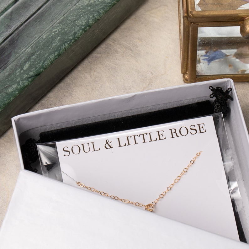 May include: A white box with a black velvet lining and a gold chain necklace inside. The box has a white card with the text "SOUL & LITTLE ROSE" printed on it.