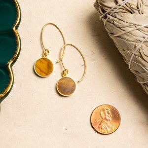 May include: A pair of gold hoop earrings with round tiger's eye stone accents.