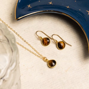 May include: A gold necklace and earrings set with teardrop-shaped tiger's eye stones.
