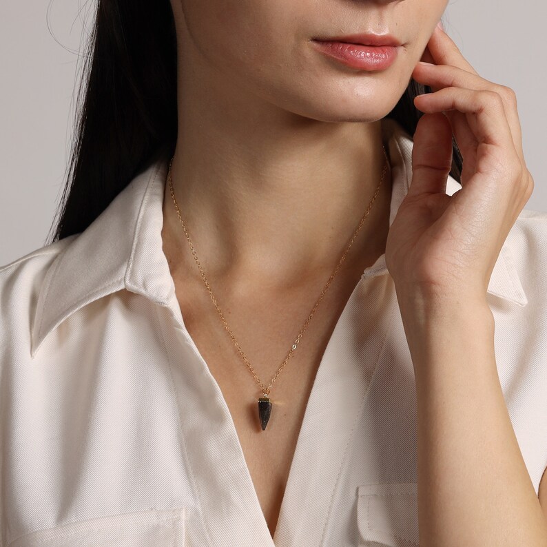 May include: A gold chain necklace with a small, dark grey, pointed pendant.