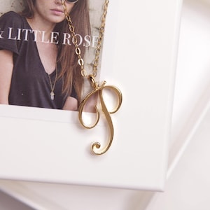 May include: A gold chain necklace with a cursive letter 'P' pendant.