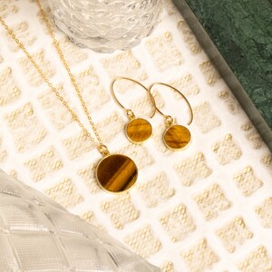 May include: A gold necklace and earrings set with tiger's eye stone pendants. The round pendants have a brown and gold color.